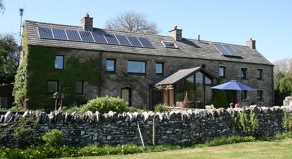 Solar thermal collectors on the right and solar PV panels on the left of a stone-built home